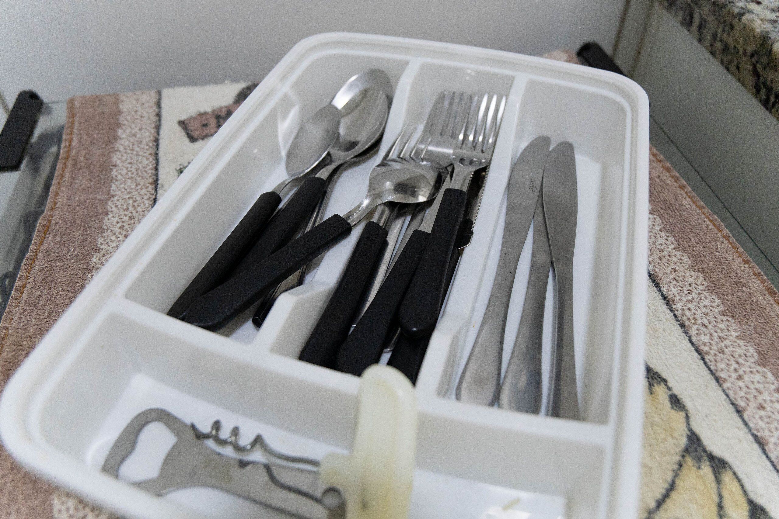Un recipiente de plástico con varios utensilios, como una cuchara, un tenedor, un cuchillo y un abrelatas.