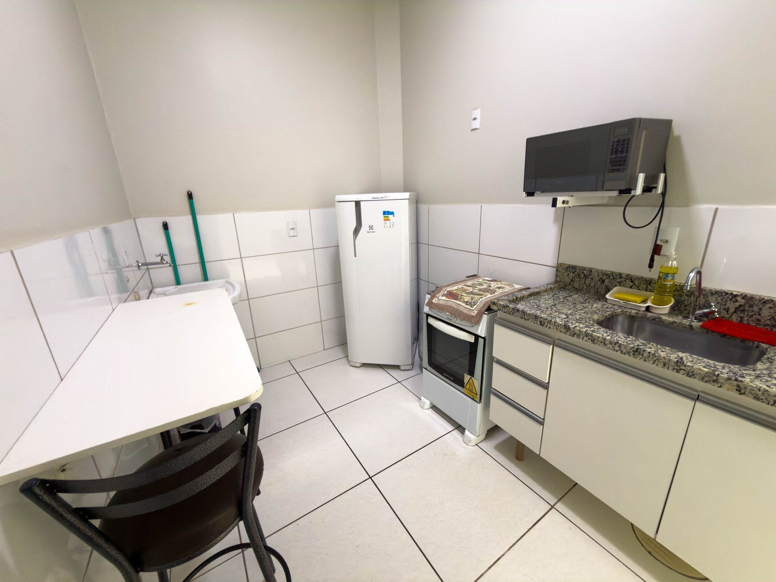 Una cucina compatta con un piano di lavoro bianco, un piccolo frigorifero, un forno a microonde e un lavello con schienale in granito.