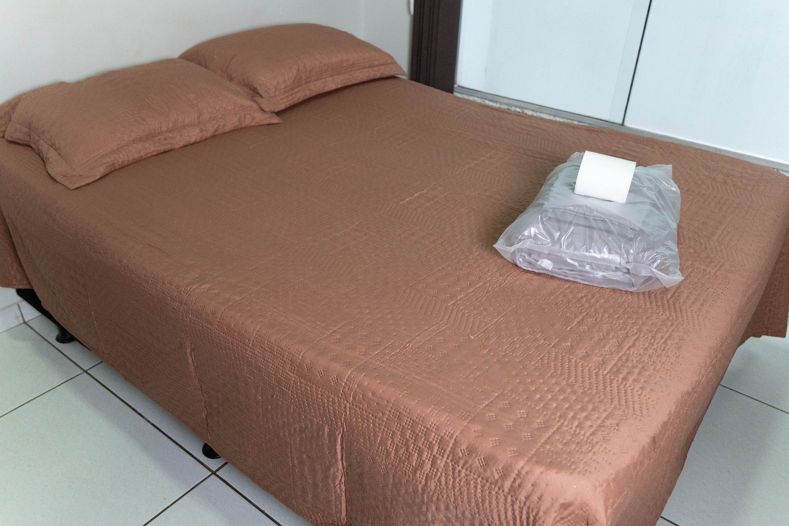 Una cama individual con una cubierta marrón y una bolsa plástica encima.