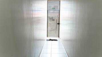 Um corredor com uma porta no final, piso ladrilhado e um portão de metal com uma placa em cima.