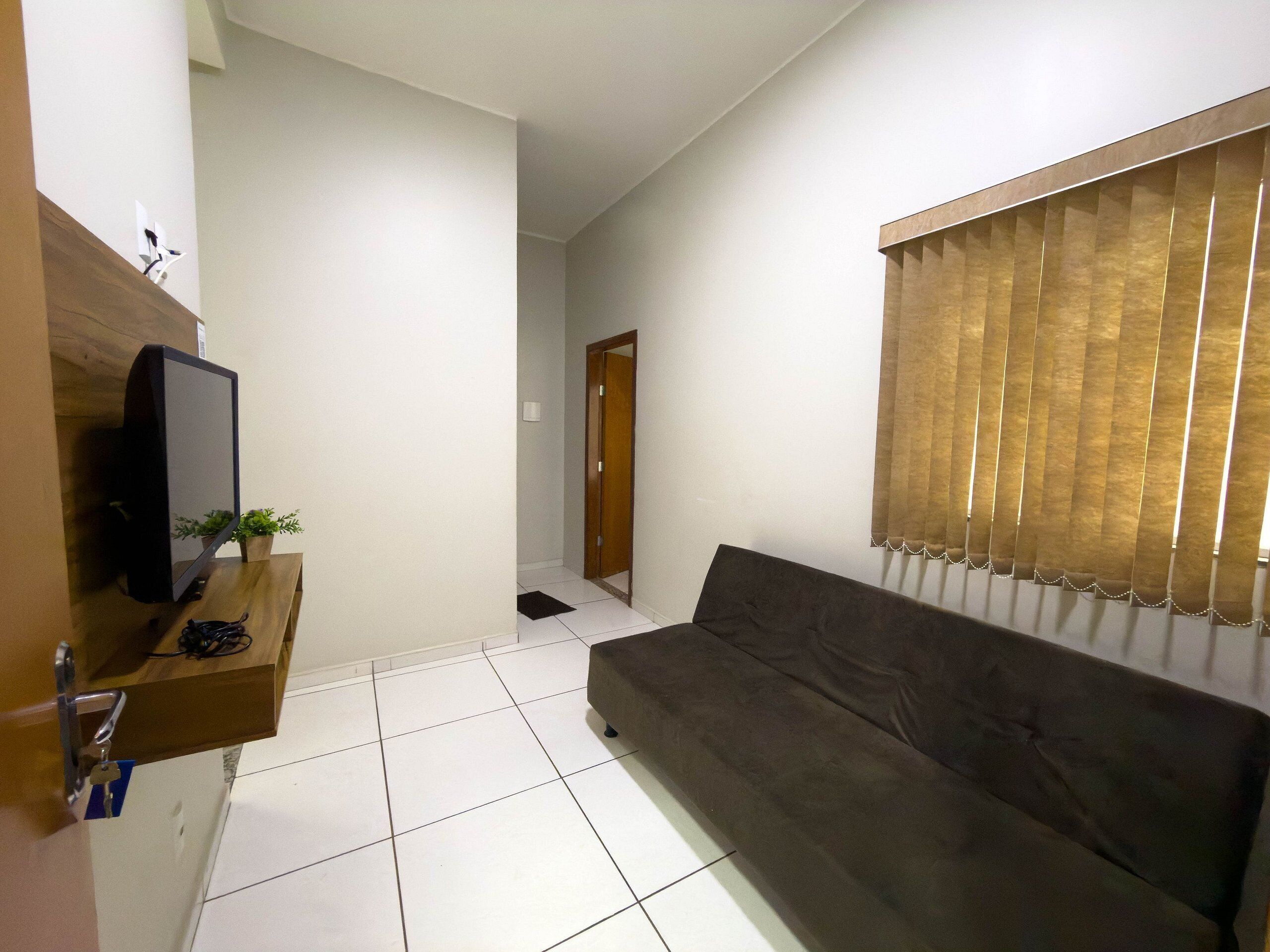 Una sala de estar con un sofá, un televisor sobre un mueble bajo, una estantería de madera y una ventana con persianas.