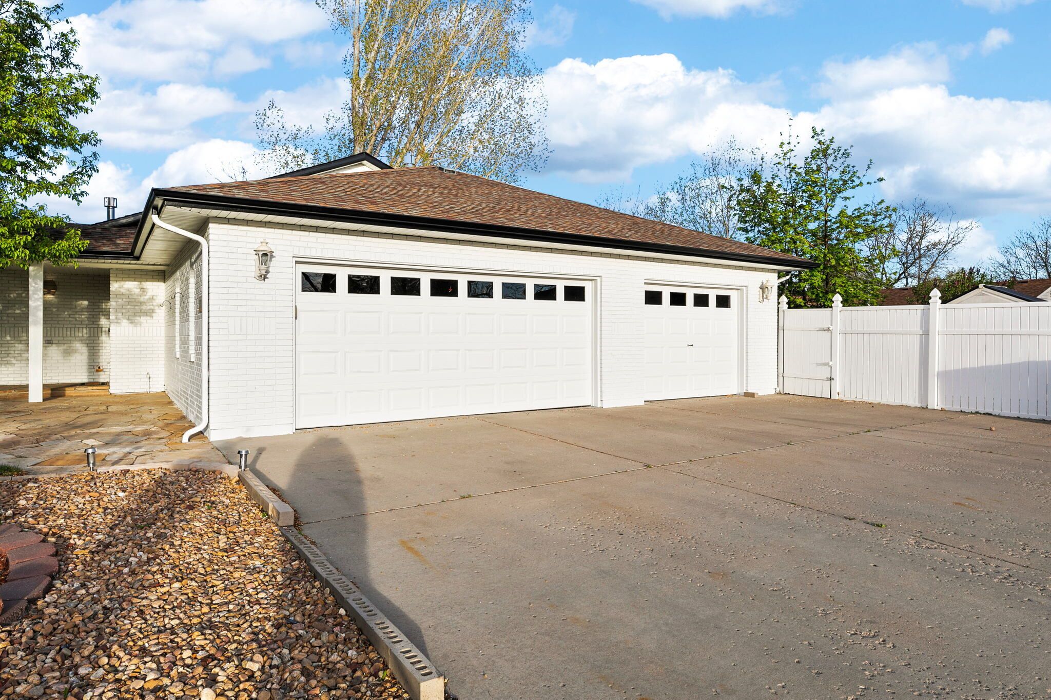 A single-story house with a garage, a stone-paved driveway, and a white picket fence.