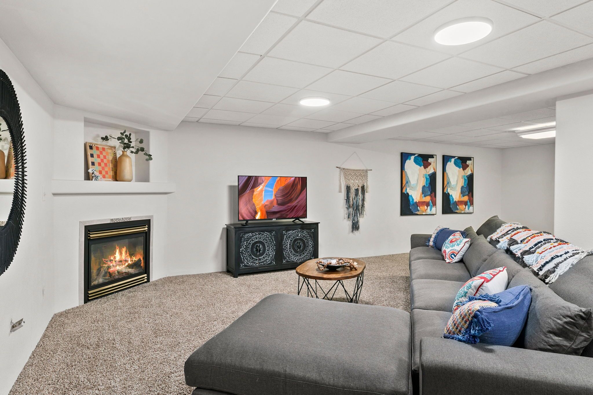 A modern living room with a fireplace, a large flat-screen TV, a gray sofa, and decorative pillows.