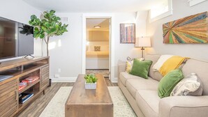 A living room with a TV, wooden entertainment unit, sofa, and a plant. - Cozy Retreat | Walk to Unc | Free Cruiser Bikes (Greeley)