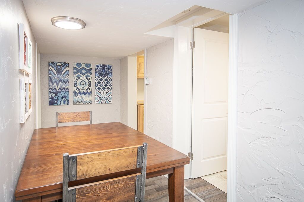 A dining area with a wooden table and chairs, patterned wall art, and a white door.
