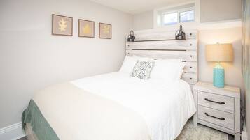 Un dormitorio con cama, mesita de noche, lámpara y una obra de arte con hojas enmarcada en la pared.