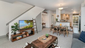 Un soggiorno moderno con una televisione a schermo piatto, un tavolino in legno e una zona pranzo con tavolo e sedie in vetro.