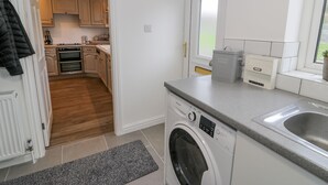 A modern kitchen with wooden flooring, a built-in oven, a washing machine, and a window with a view.