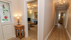A hallway with wooden flooring, a door with a floral glass panel, a lamp, and a television in the background.