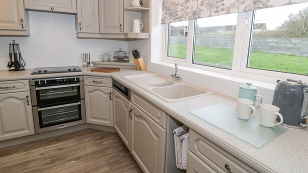 A kitchen with white cabinetry, a double sink, and a window with a view of a green landscape.