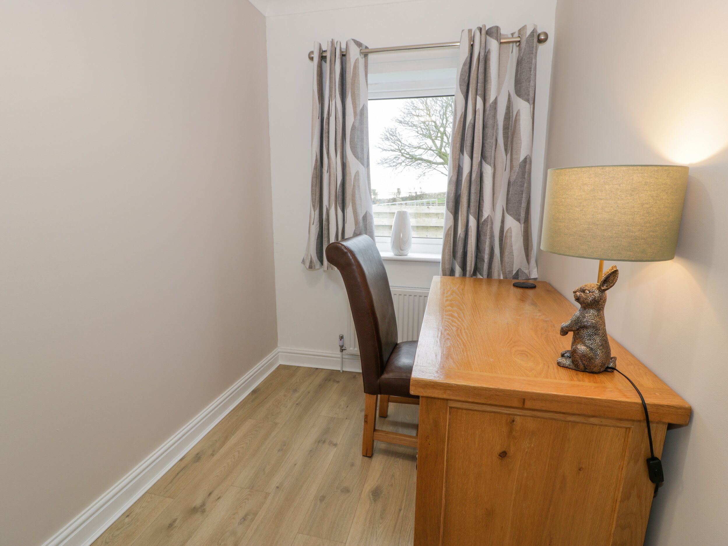 A room with a wooden desk, a chair, a lamp, and a window with curtains.