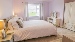 A bedroom with a bed, bedside tables, a dresser, a wardrobe, and a window with curtains.