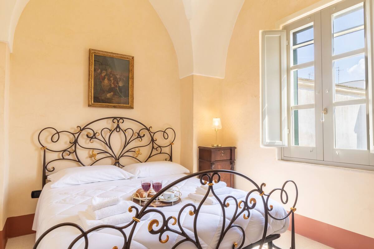 A neatly made bed with a tray of breakfast items, a bedside lamp, and a painting on the wall.