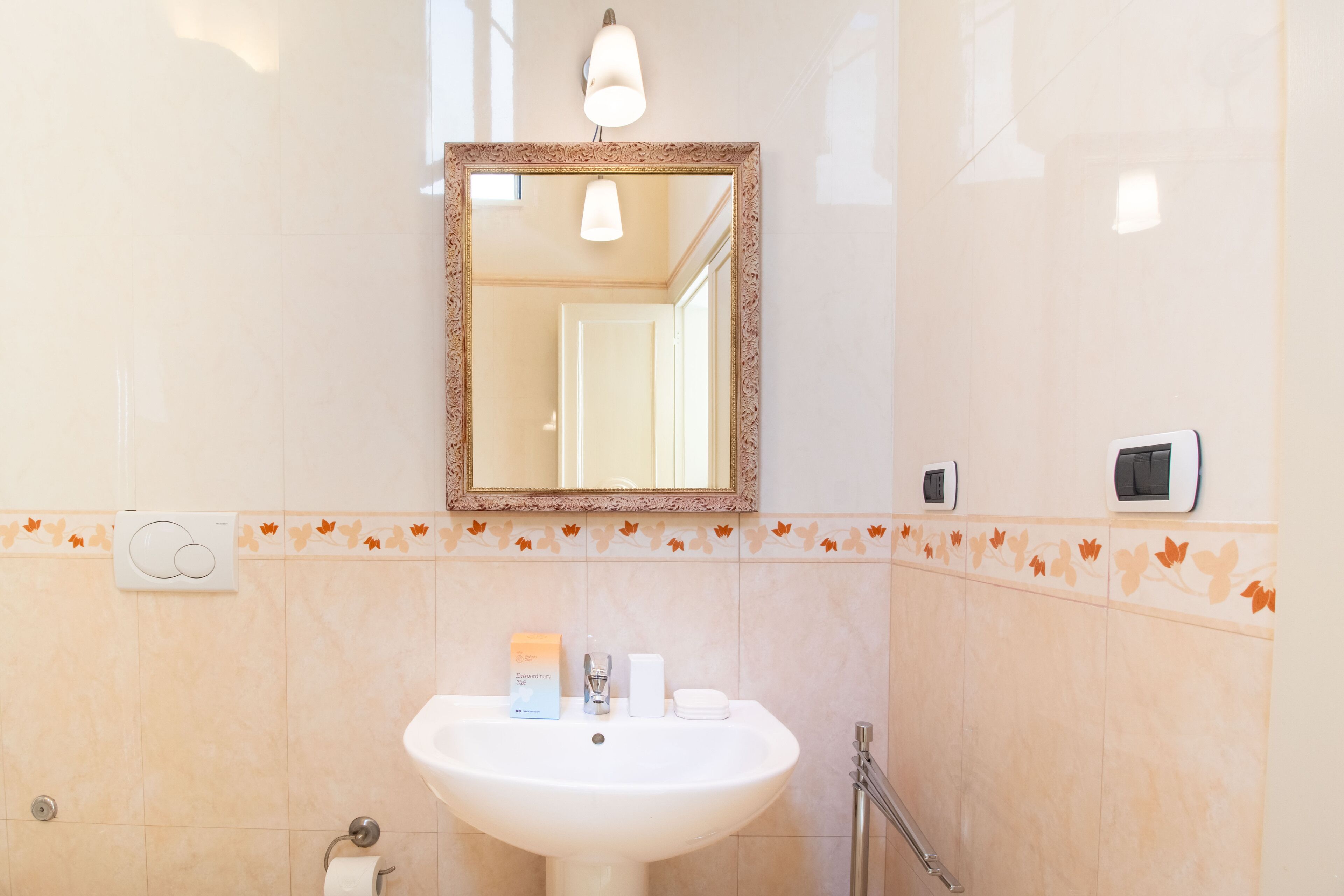 A bathroom with a white sink, a mirror, a towel dispenser, and a toilet paper holder.