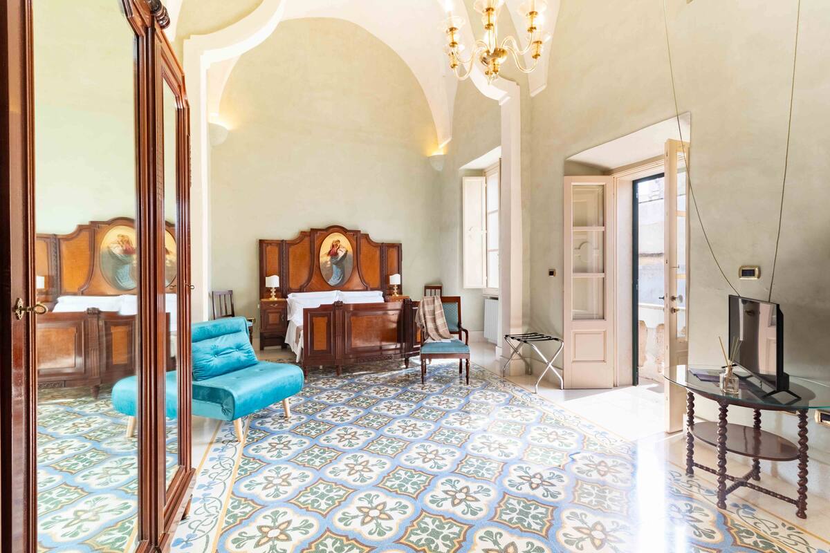 A spacious room with a large bed, a blue sofa, a wooden headboard, and a patterned floor.
