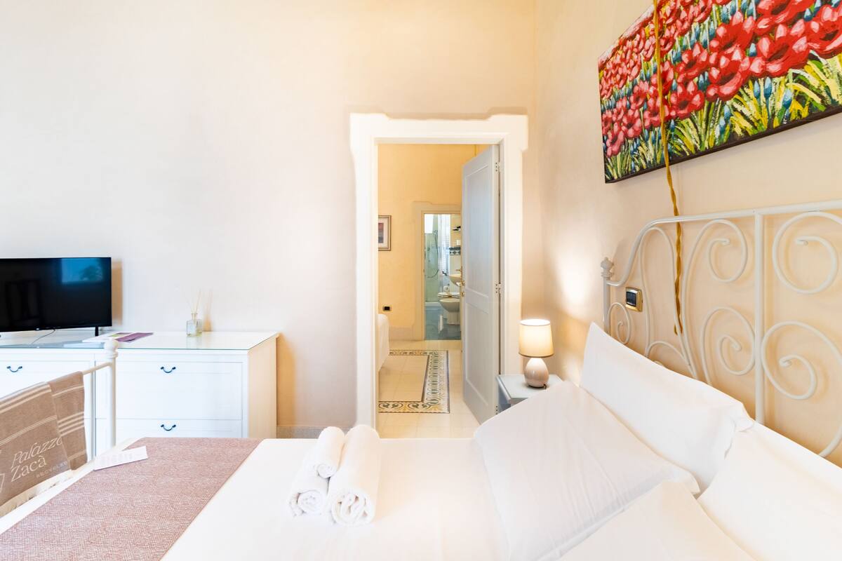 A hotel room with a bed, a TV, a desk, and a bathroom visible through an open door.