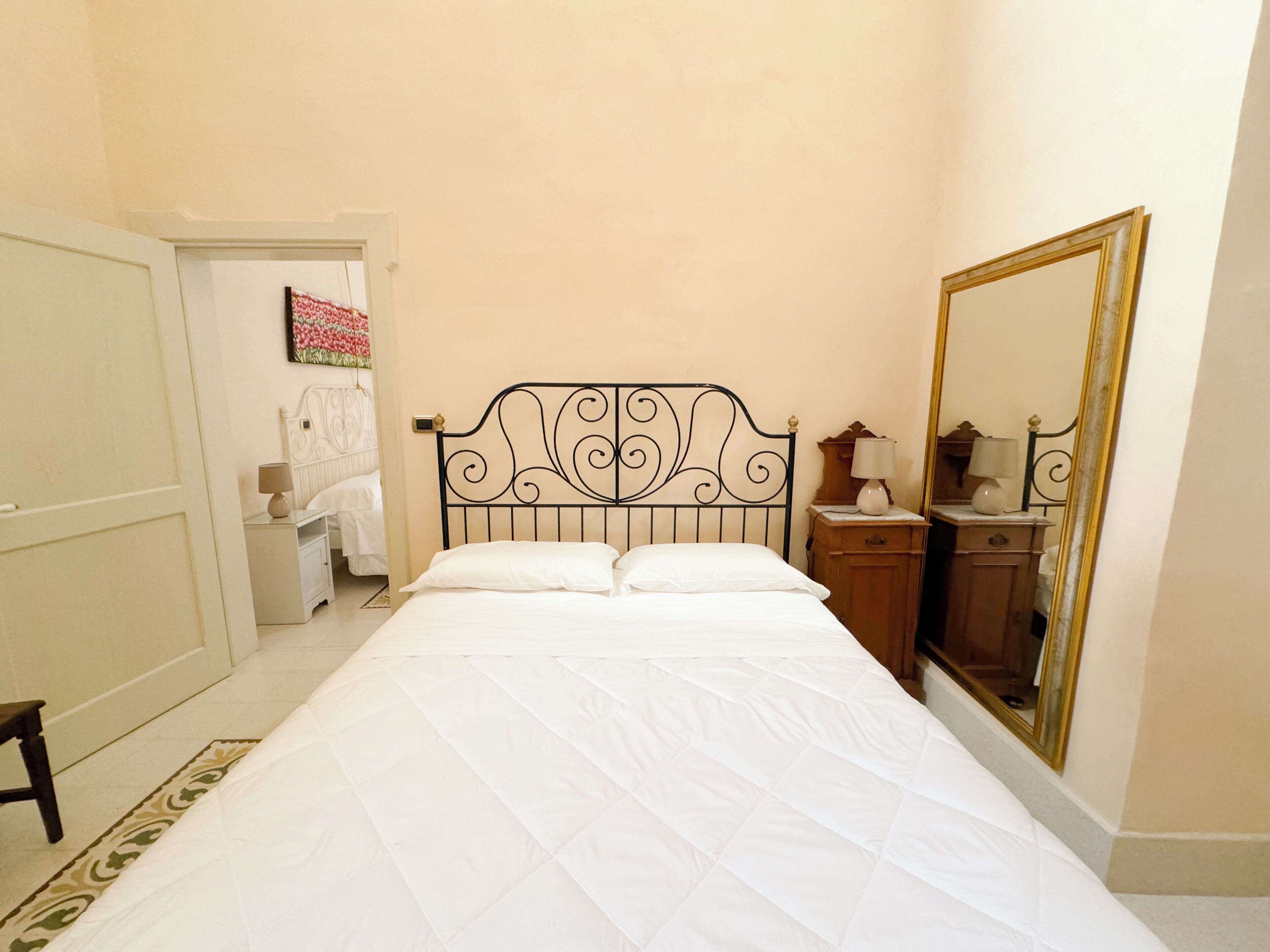 A neatly made bed with a headboard, a bedside table with a lamp, and a large mirror on the wall.