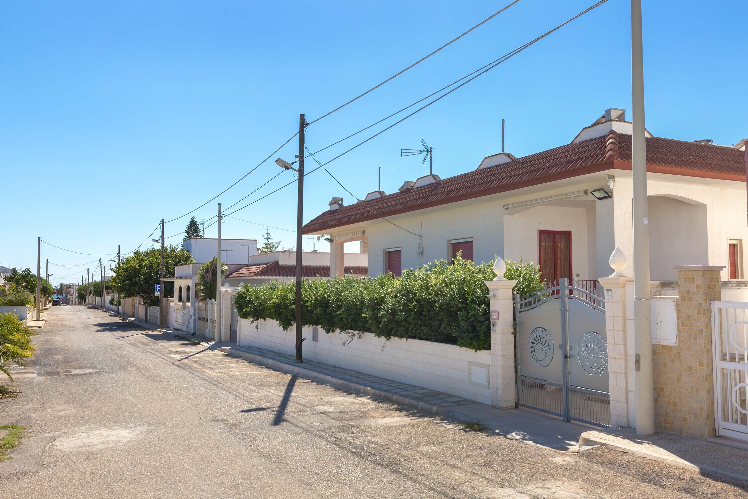 A residential street with houses, a gated entrance, and a clear sky.