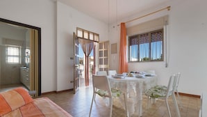 A room with a dining table set for four, a sofa, a window with curtains, and a door leading to another room. - 3150 Villa Giovì - Appartamento 2 by Barbarhouse (Manduria)
