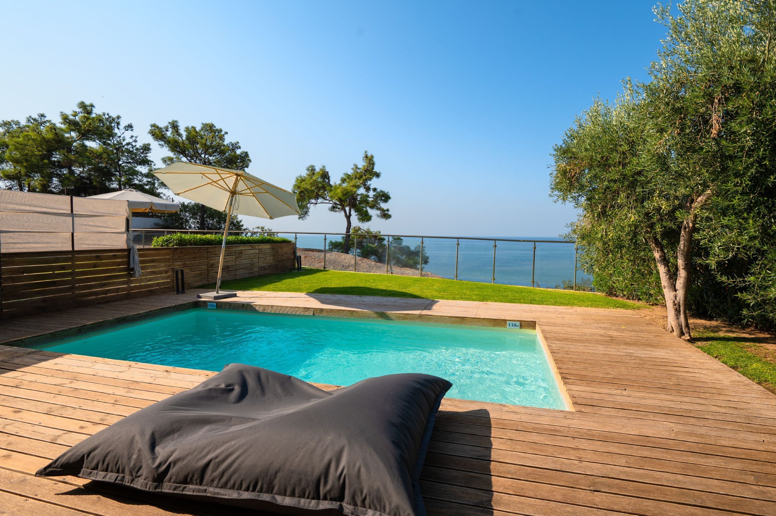 En træterrasse med pool, liggestol og havudsigt.