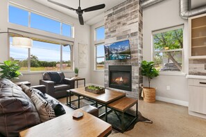 A spacious living room with a fireplace, large windows, and a ceiling fan. - Old Town Modern New Build: Rftp Spa W/ Mtn Views! (Fort Collins)
