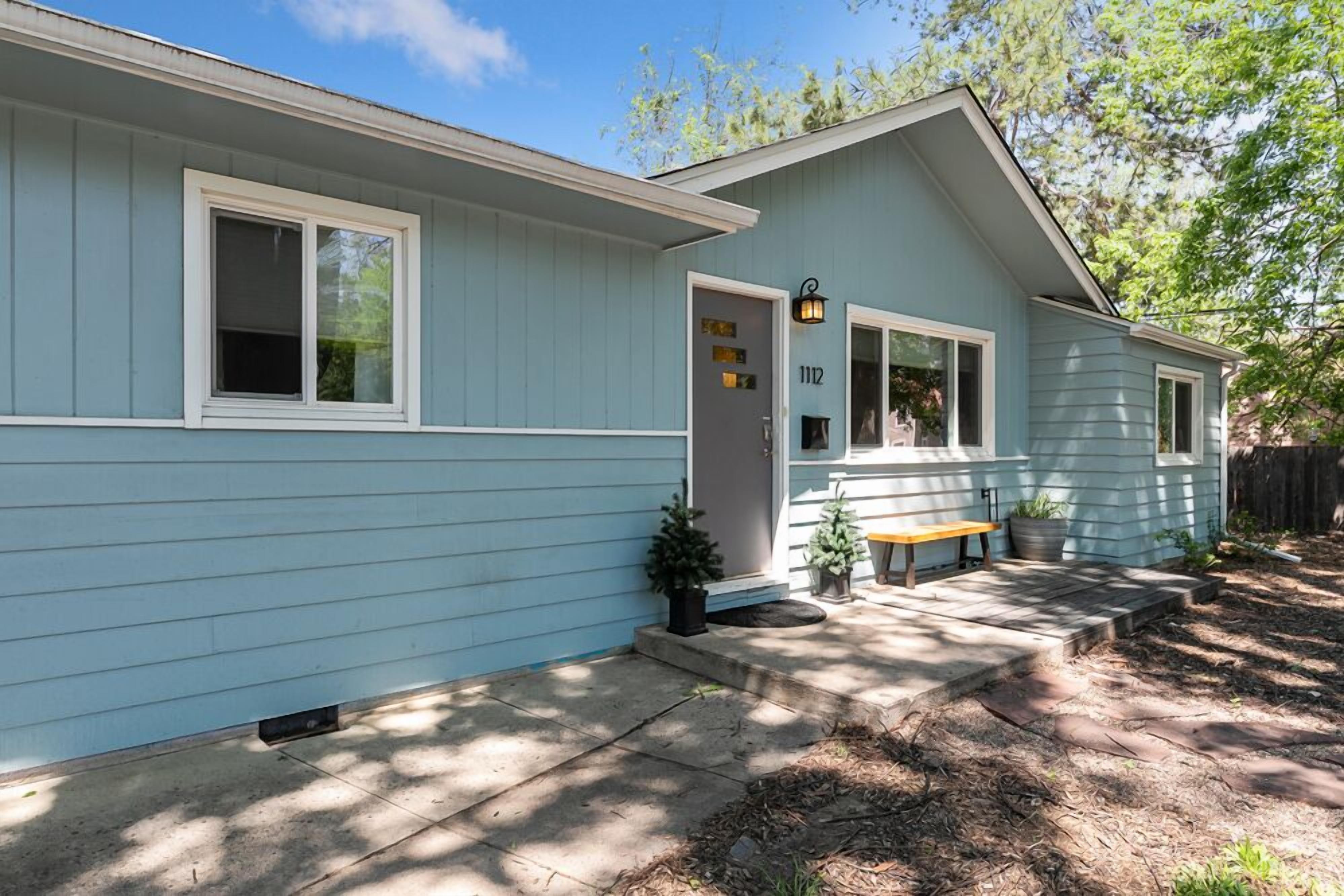 A light blue single-story house with a front porch, a mailbox, and a number 112 sign.