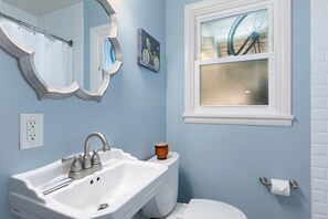 A bathroom with a white sink, a mirror, a toilet, and a window with a bicycle painting. - Fun, Family-friendly Old Town Home W/ Hot Tub! (Fort Collins)