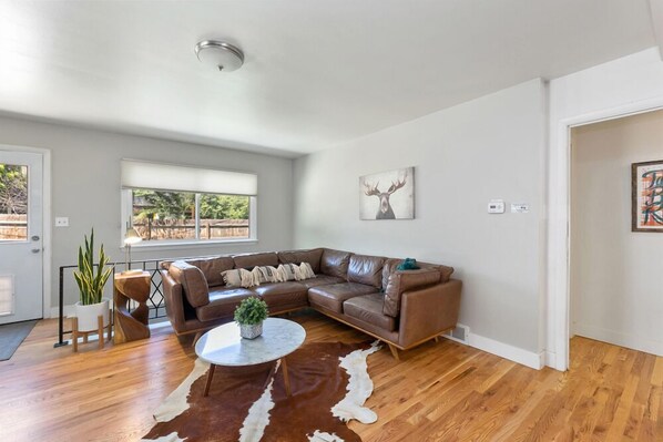 A modern living room with a brown leather sectional sofa, a round coffee table, and a cowhide rug. - Fun, Family-friendly Old Town Home W/ Hot Tub! (Fort Collins)