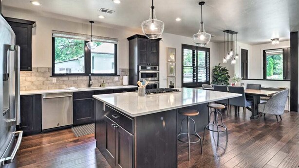 A modern kitchen with dark cabinetry, a large island, and pendant lighting.