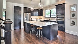 A modern kitchen with dark cabinetry, a large island with stools, stainless steel appliances, and pendant lighting.