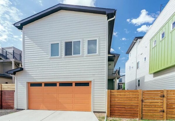A two-story residential building with a garage, a wooden fence, and a clear sky.