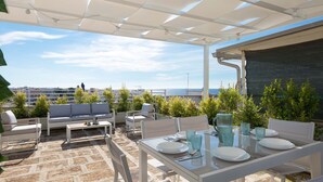 An outdoor patio with white furniture, a glass table, and a view of the sea. - 3135 La Voce del Mare by Barbarhouse (Nardò)