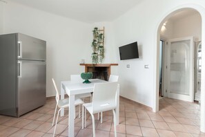 Une cuisine compacte équipée d’un réfrigérateur, d’une table à manger avec des chaises, d’un téléviseur à écran plat fixé au mur et d’une plante en pot placée sur une étagère.