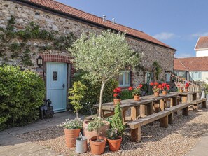 A stone building with a tiled roof, a wooden bench, and potted plants. - The Calf Pen (Colyton)