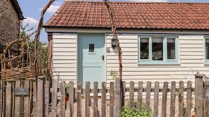 Uma casa branca com porta azul, janelas e telhado de telhas vermelhas, além de cerca de madeira.