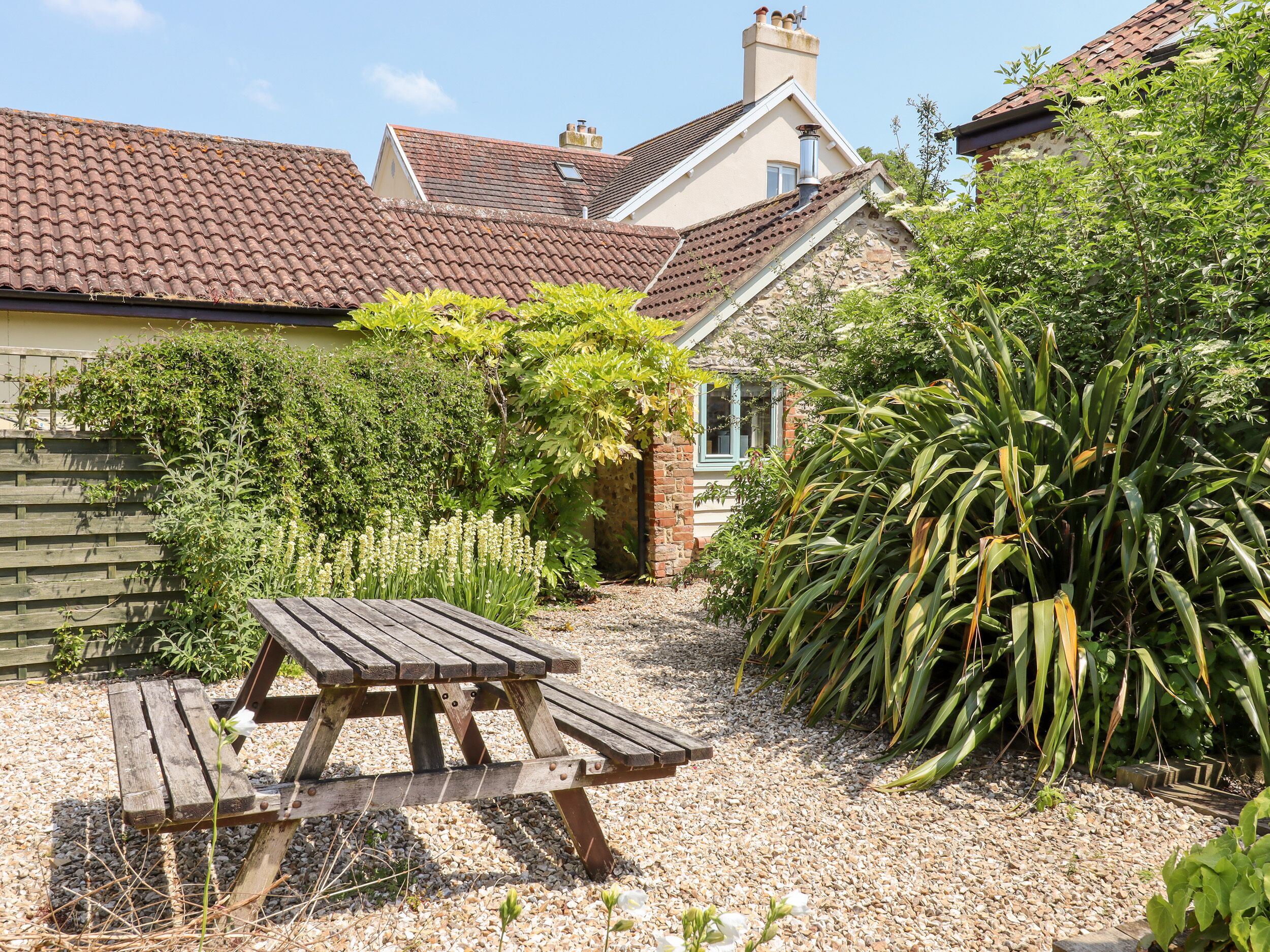 A garden with a wooden picnic table, surrounded by gravel and various plants.