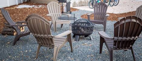 Een terras met Adirondack-stoelen, een vuurkorf en een barbecue.