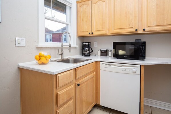 Una cocina compacta con armarios de madera, encimera blanca, un lavamanos, cafetera, microondas y lavavajillas.