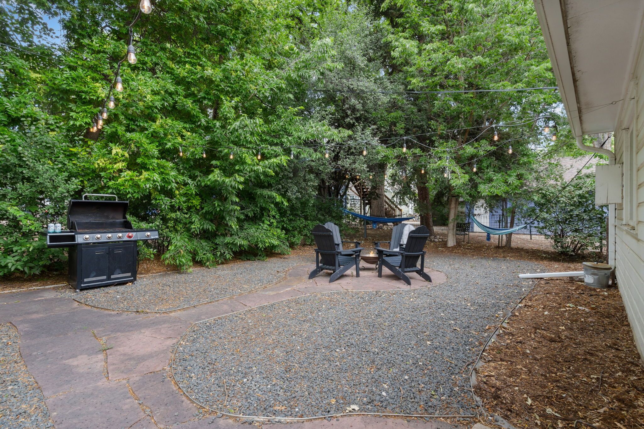 A backyard with a grill, two Adirondack chairs, and a hammock.