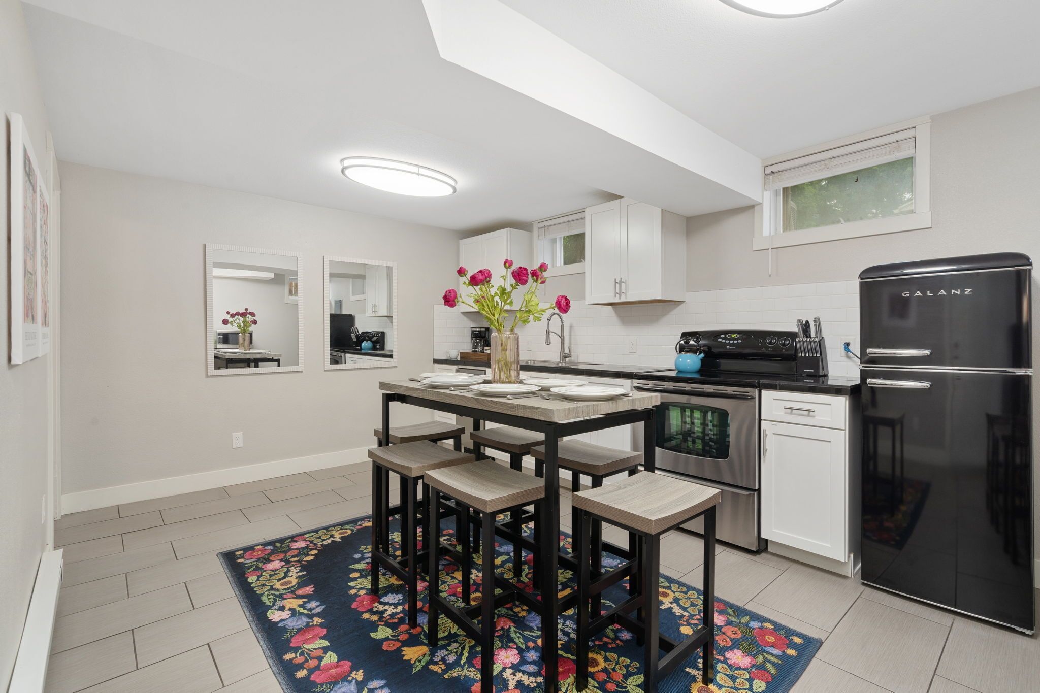 A modern kitchen with white cabinets, a black refrigerator, and a dining area with a floral rug.