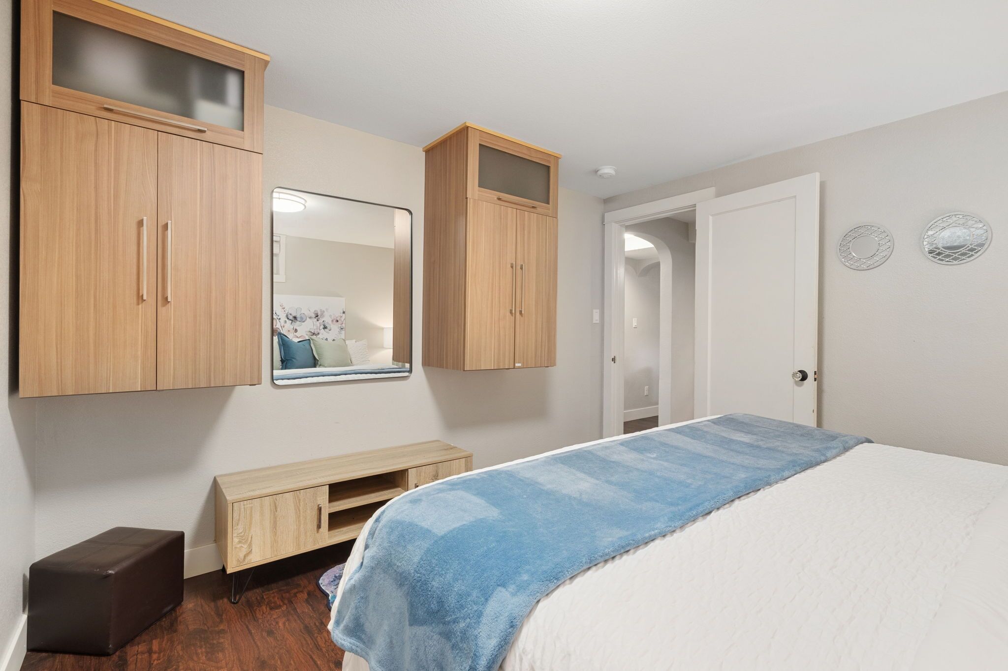 A bedroom with a bed, a wooden wardrobe, a mirror, and a door.