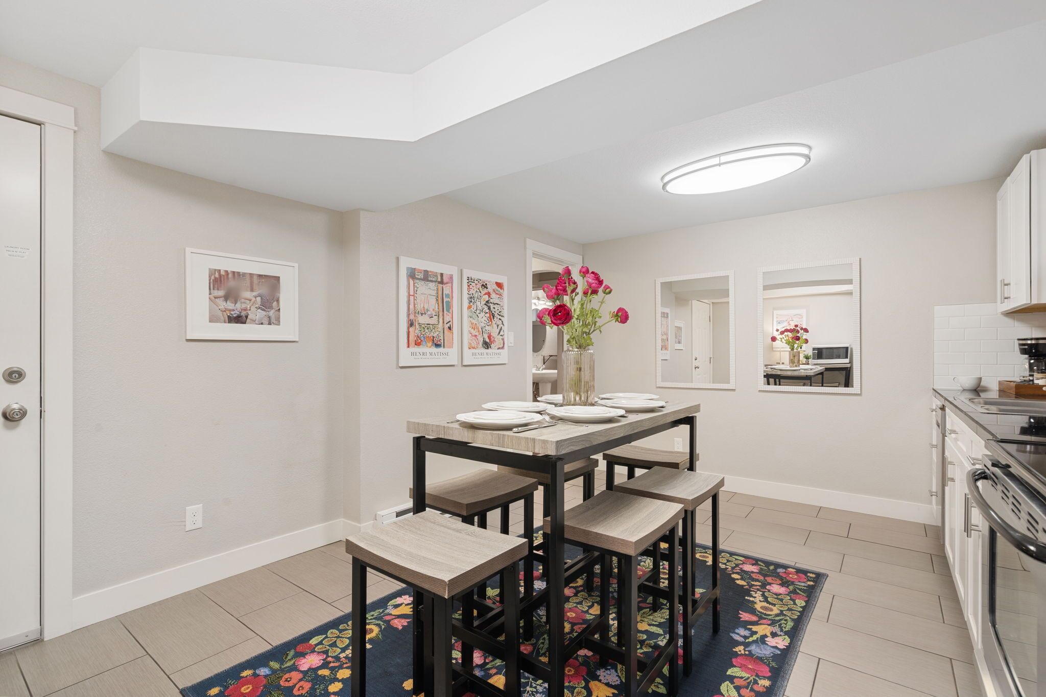 A modern kitchen with a dining area, featuring a central island, a built-in oven, and a large window.
