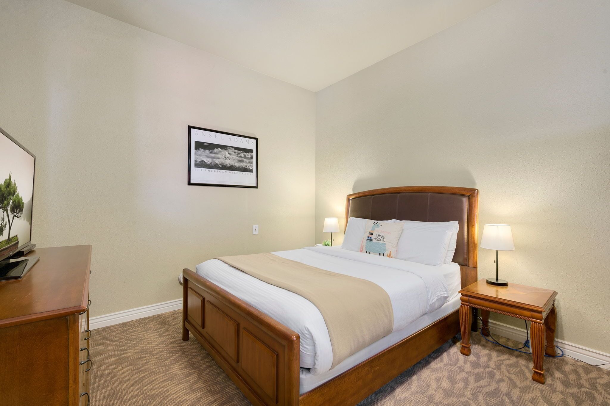 A neatly made bed with a wooden headboard, two bedside lamps, and a framed picture on the wall.