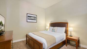 A neatly made bed with a wooden headboard, two bedside lamps, and a framed picture on the wall.