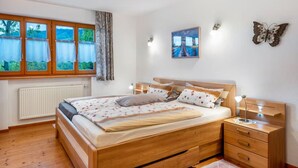 A bedroom with a wooden bed, a bedside table, a nightstand, a window with curtains, a radiator, and a wall-mounted picture. - Vacation apartment at Fuchsbühl  (Schopfheim)