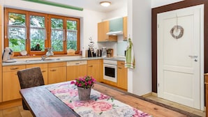 A modern kitchen with wooden cabinets, a dining table with a floral table runner, and a view of greenery outside. - Vacation apartment at Fuchsbühl  (Schopfheim)