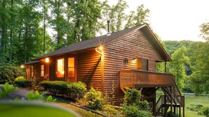 Une cabane en bois dotée d’un balcon et d’un escalier menant à une terrasse, le tout entouré d’une végétation luxuriante.