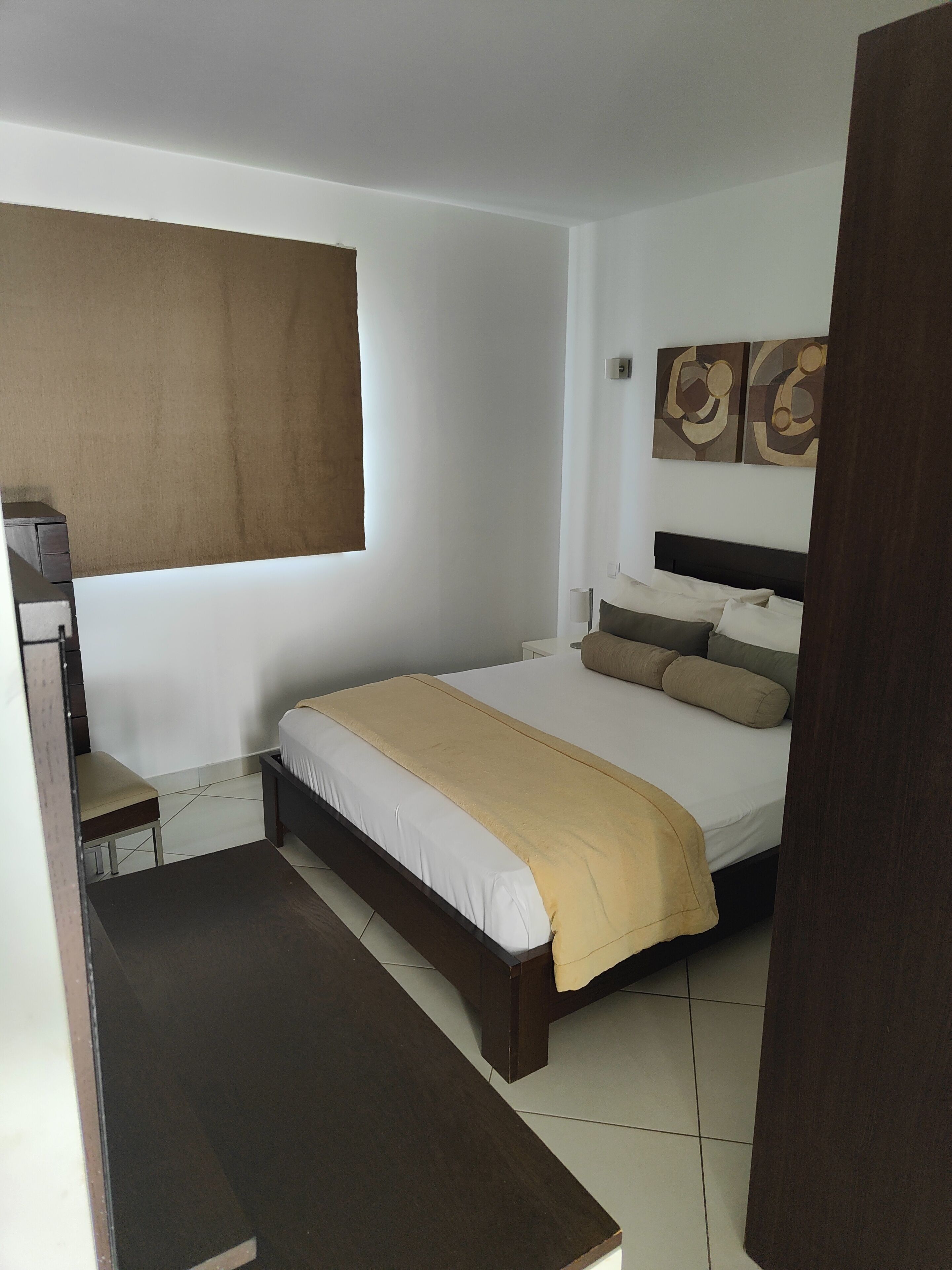 A bedroom with a bed, a desk, and a window with a blind.
