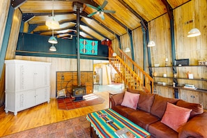 A cozy living room with a brown leather sofa, a patterned rug, and a wooden ceiling.