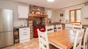 A kitchen with a brick wall, white cabinets, a wooden table, and a refrigerator.